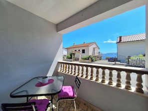 Een balkon met een tafel en stoelen, een stenen muur en uitzicht op een gebouw met een rood dak.