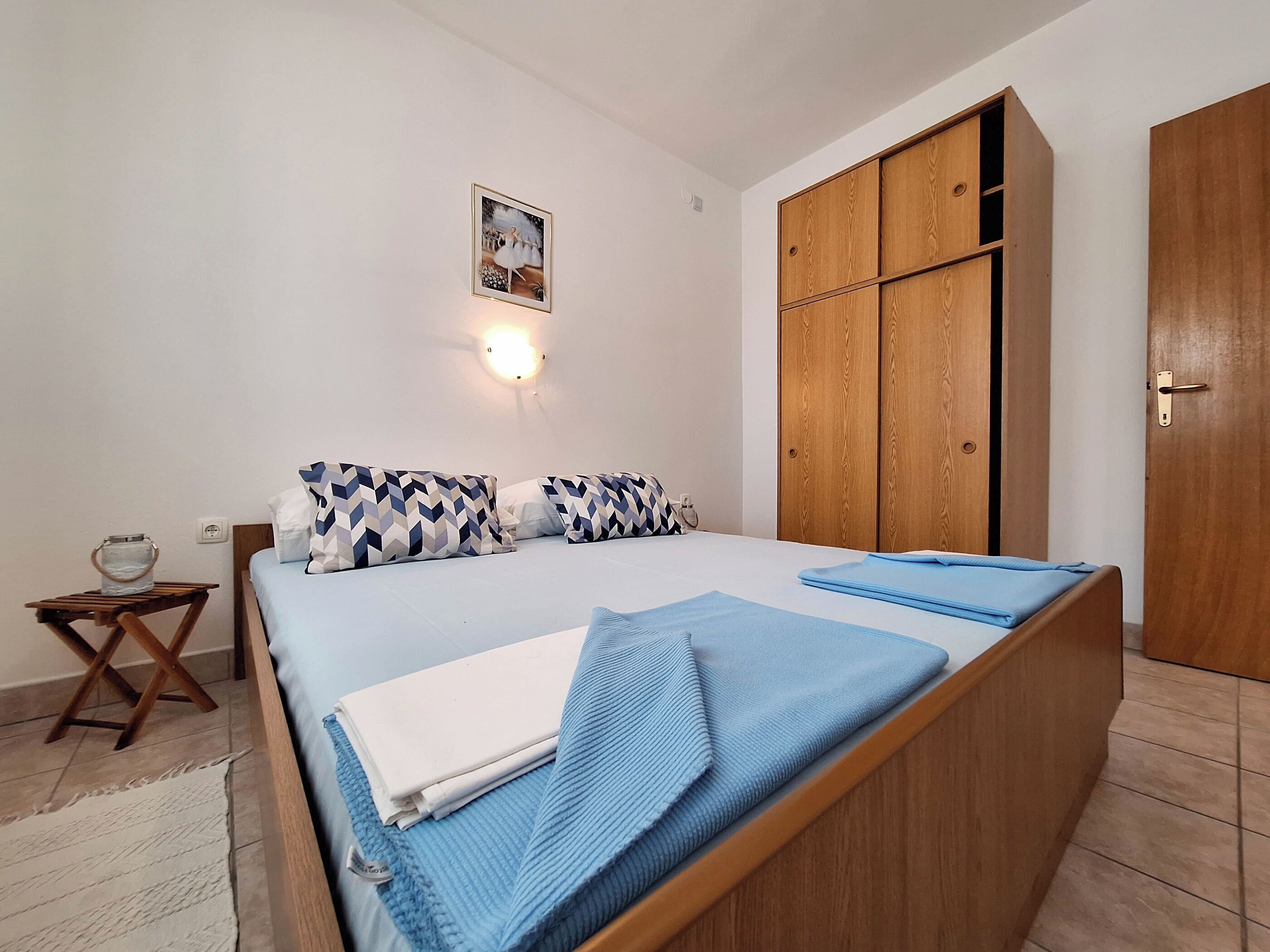 Une chambre à coucher comprenant un lit, une armoire en bois, une petite table et un luminaire fixé au mur.