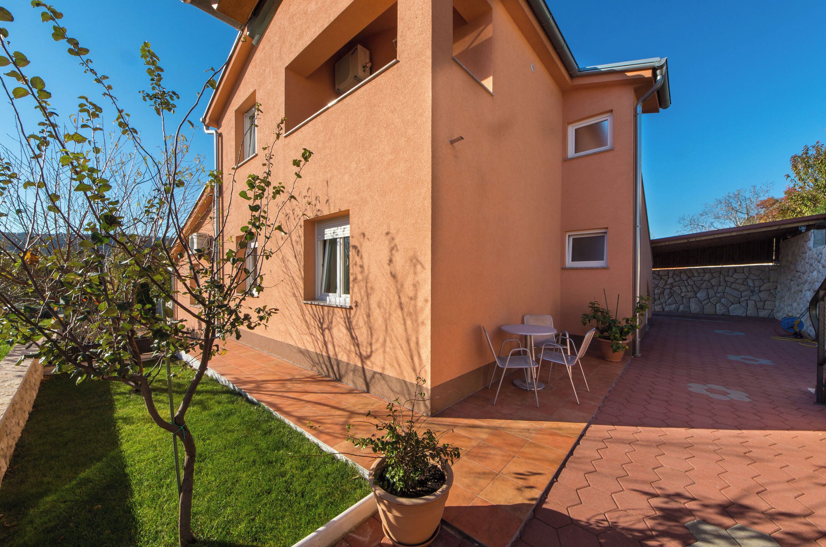 Un bâtiment à deux étages avec une façade en pierre, un petit patio avec une table et des chaises, et une plante en pot.