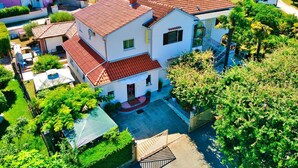 Ein zweistöckiges Haus mit rotem Ziegeldach, umgeben von Grünflächen und weiteren Wohnhäusern.