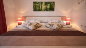 Ein ordentlich bezogenes Bett mit braunem Kopfteil, zwei Nachttischlampen und einem Wandbild mit Waldmotiv.