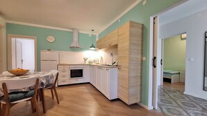 Ett kompakt kök med vita skåp, en inbyggd ugn och en matplats med ett bord och stolar.