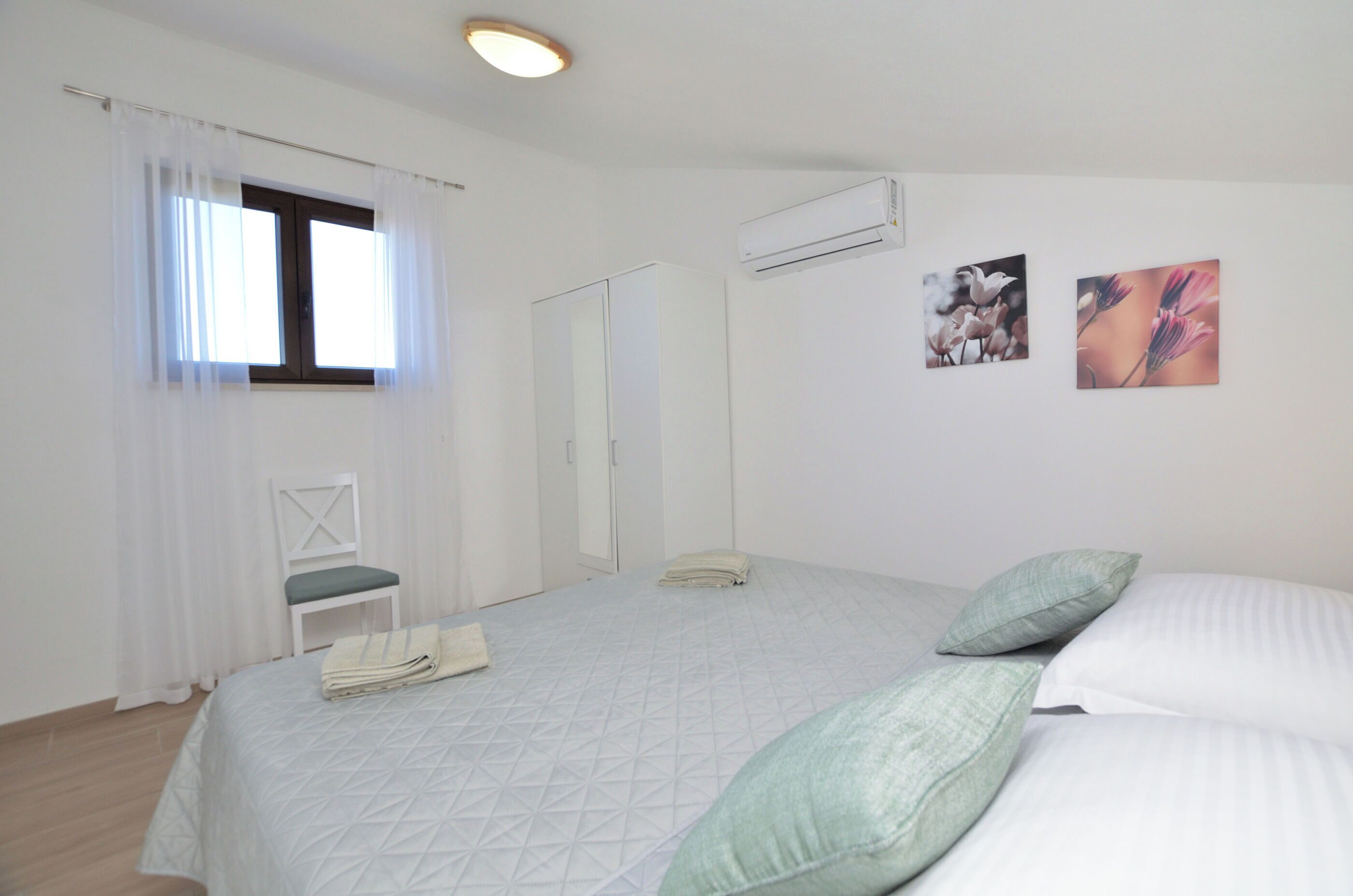 A bedroom with a bed, a chair, and two wall-mounted air conditioning units.