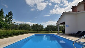A swimming pool with a clear blue sky, surrounded by greenery and a building with a tiled roof. - House Danci (Vizinada)