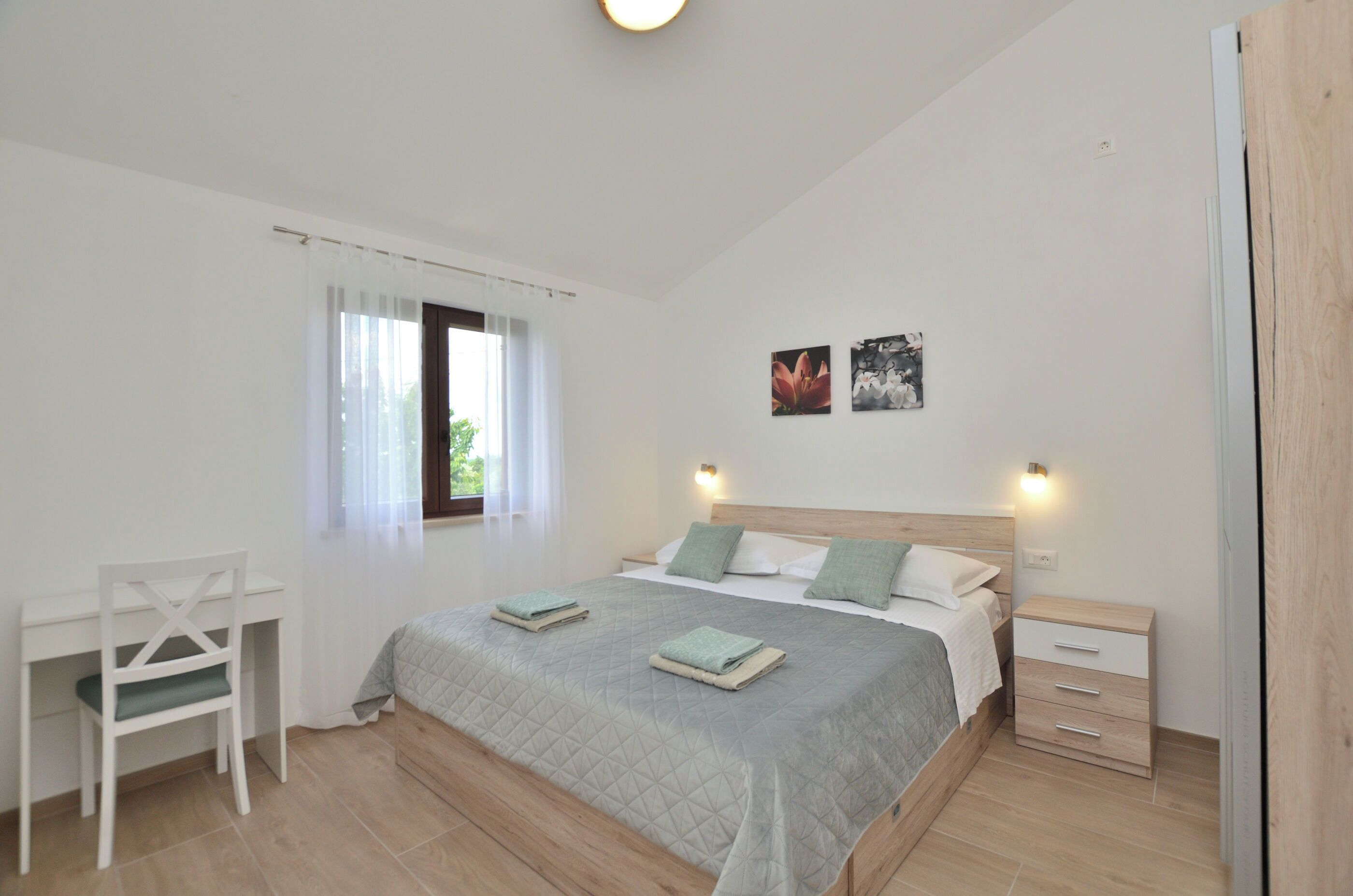 Een slaapkamer met een bed, een bureau en een stoel. Twee wandlampen en een raam met gordijnen.