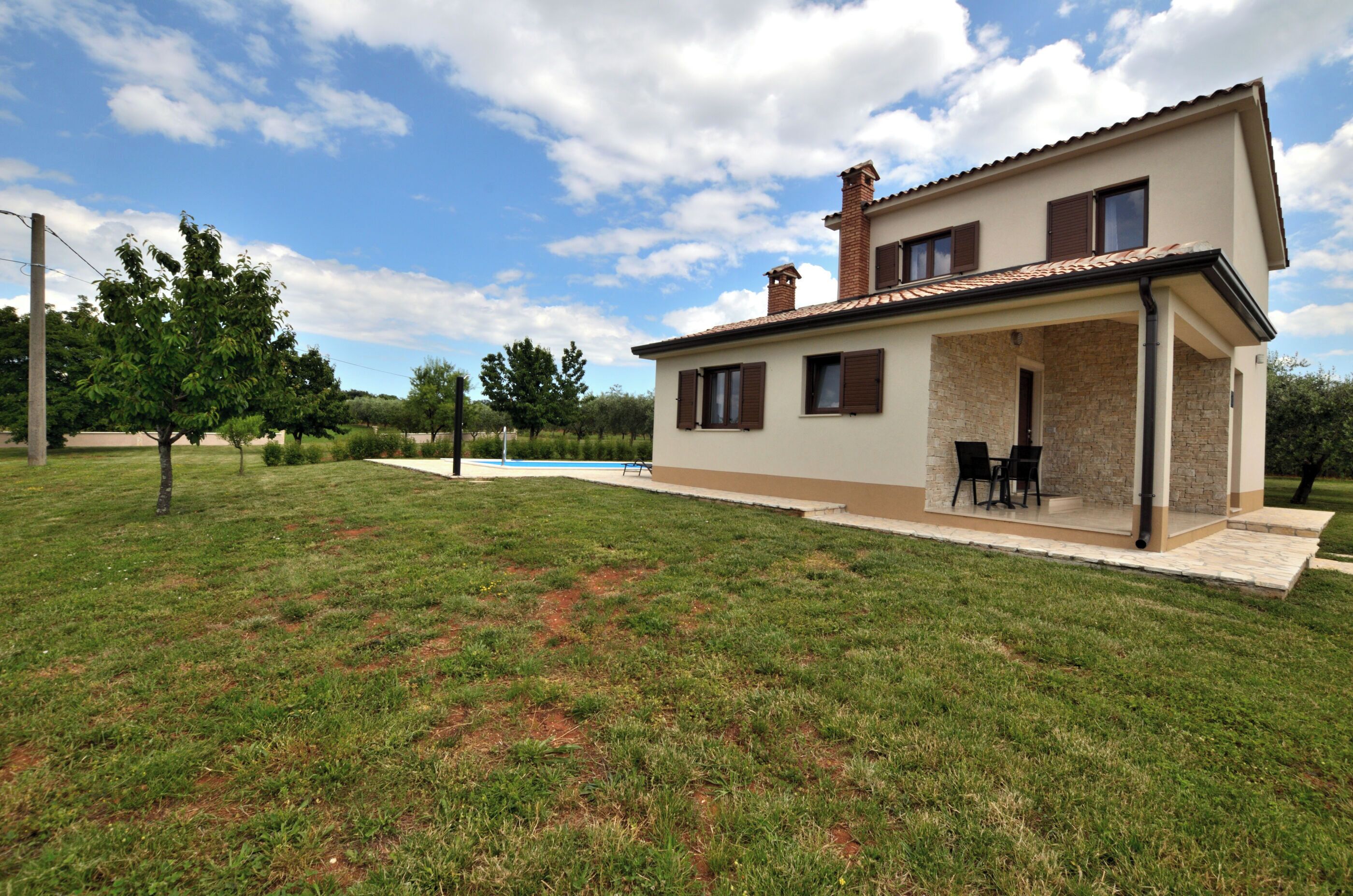A two-story house with a covered patio and a swimming pool in the background.
