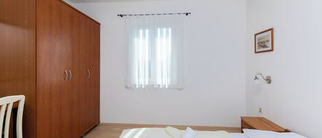 Een slaapkamer met een bed, een houten garderobe, een stoel, een nachtkastje, een lamp en een raam met gordijnen.