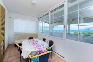 En balkon med et bord og stole, en sofa, samt hav- og bjergudsigt.