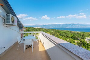 A balcony with a table and chairs, overlooking a coastal landscape with trees and the sea. - Apartments Ivan M (Lopar)