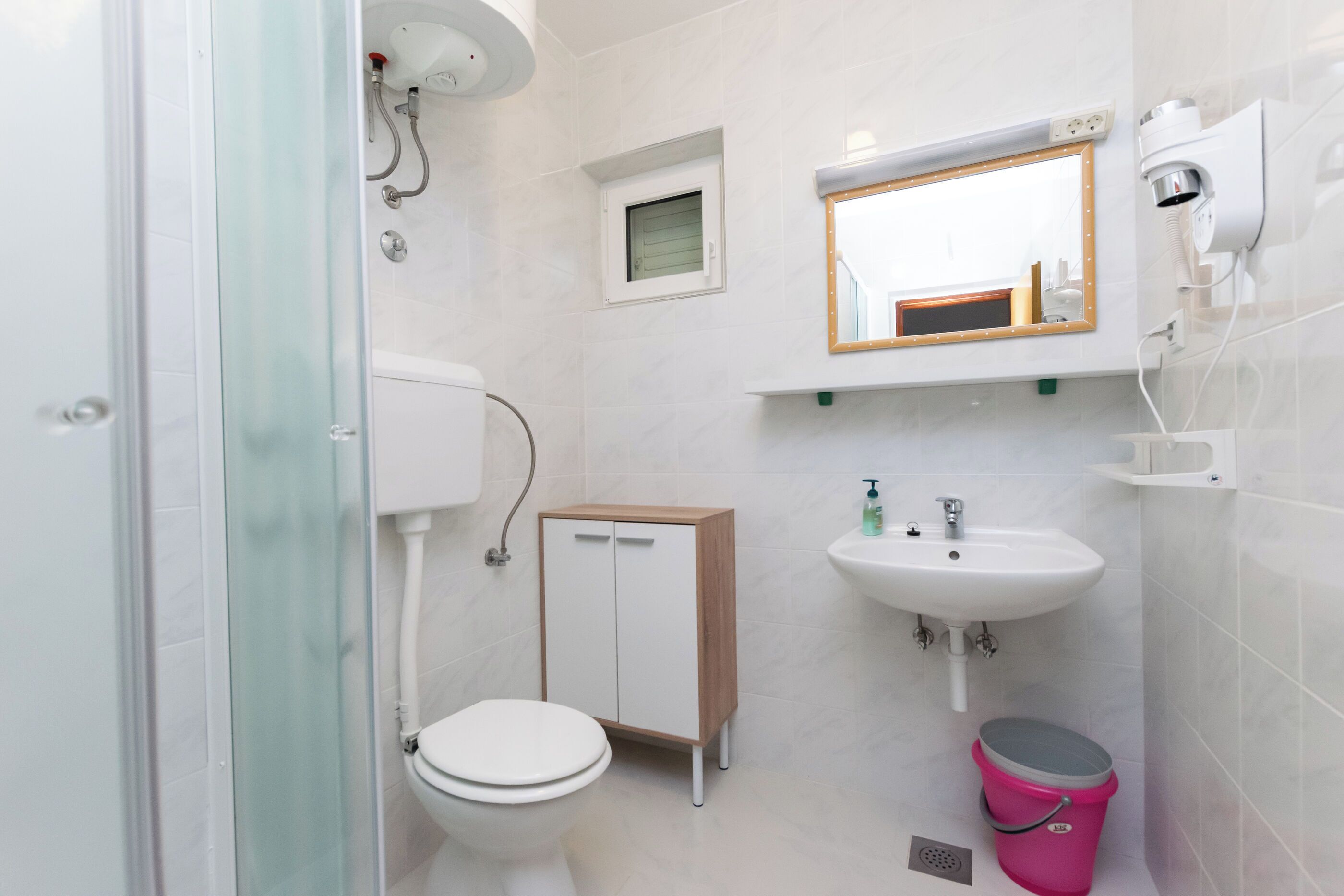 A bathroom with a toilet, a cabinet, a sink, a mirror, and a shower.