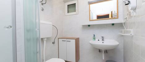 A bathroom with a toilet, a cabinet, a sink, a mirror, and a shower.