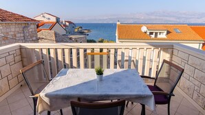 A balcony with a table and chairs, overlooking a coastal view with buildings and a sea. - Apartment Vito (Postira)