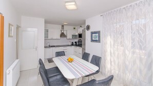 A compact kitchen with white cabinets, a central island, and a dining area with a striped tablecloth and four chairs. - Apartment Vito (Postira)
