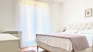 A bedroom with a bed, a bedside table, a lamp, and a window with sheer curtains. - Apartment Vito (Postira)