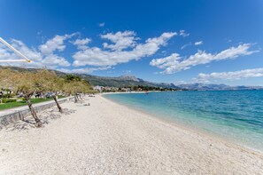 A beach with clear blue water, pebbly shore, and mountains in the background. - Apartment Stone Apartment in Center (Kastela)