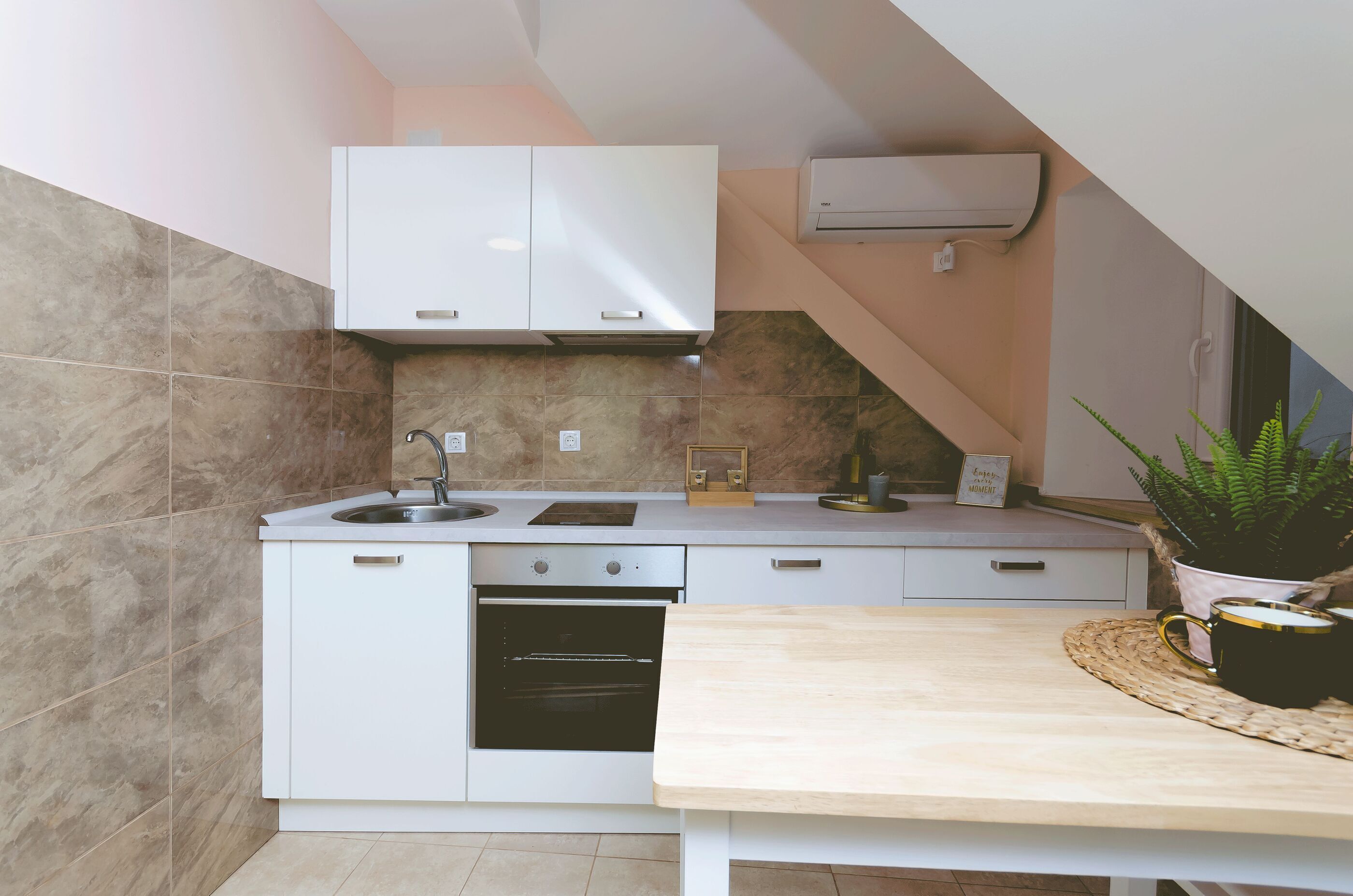 Een compacte keuken met een spoelbak, fornuis en oven, witte kasten en een klein aanrecht.