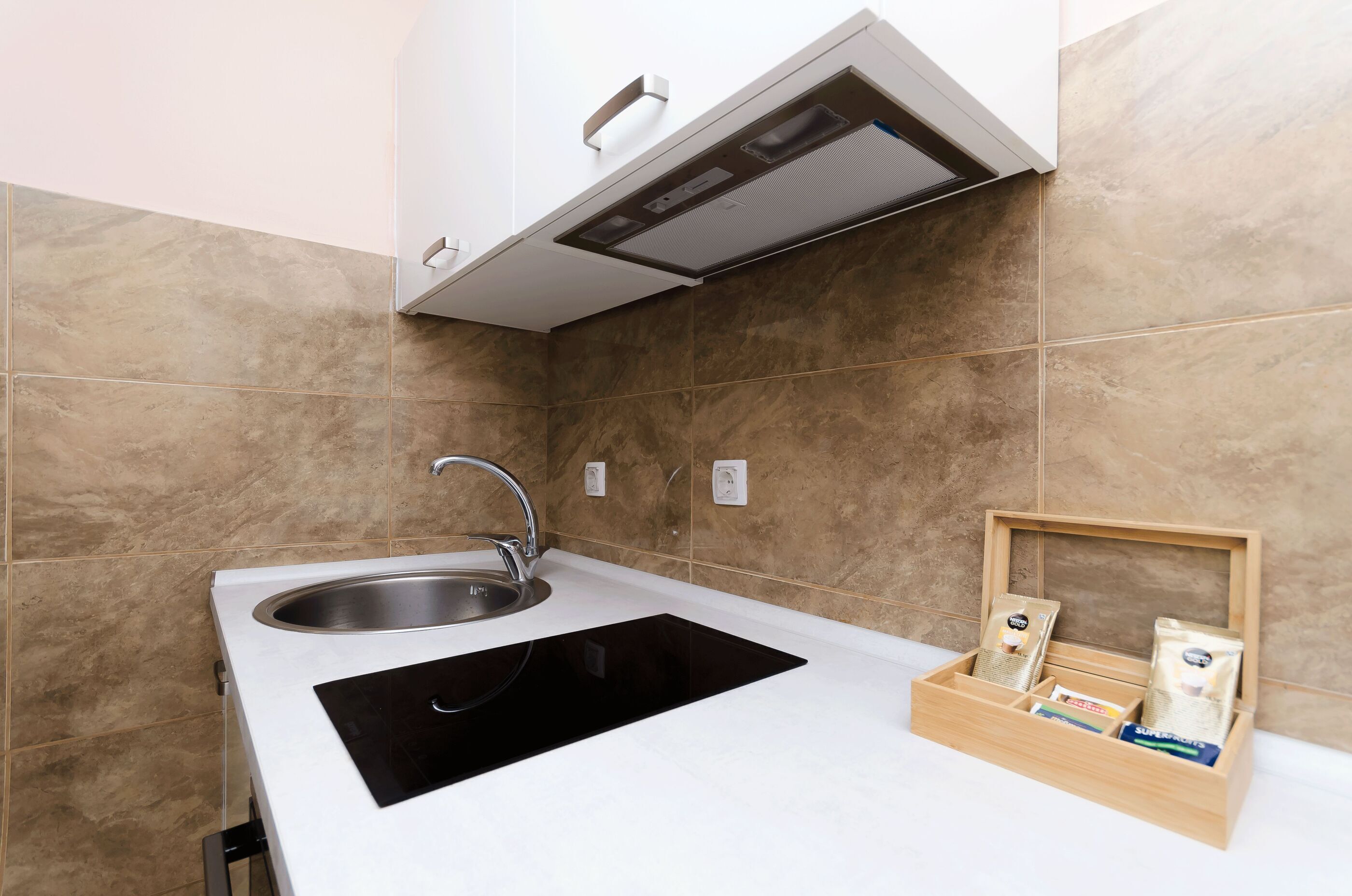 Eine moderne Küche mit integriertem Spülbecken, einer schwarzen Kochplatte und einer Holzkiste mit Küchenutensilien.