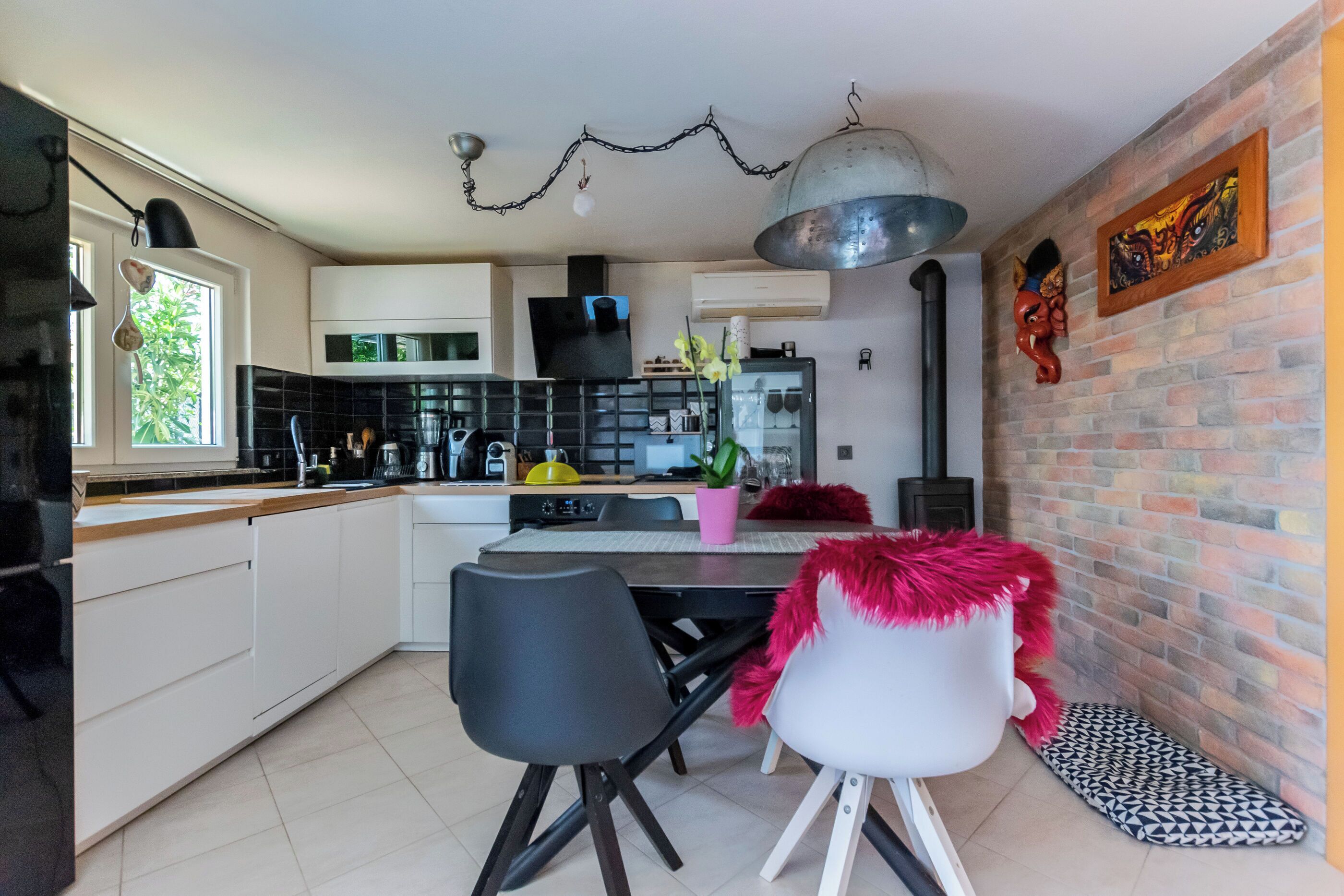 Una cocina moderna con armarios blancos, un comedor con sillas negras y blancas, y una pared de ladrillo decorada con obras de arte.