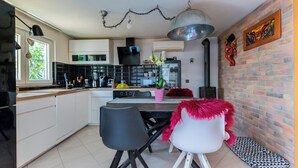 Een moderne keuken met witte kasten, een eethoek met zwart-witte stoelen en een bakstenen muur met kunstwerken.