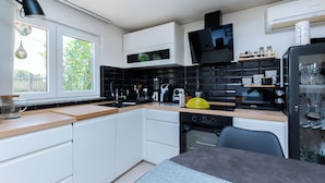 Een moderne keuken met witte kasten, een zwarte achterwand en een raam met uitzicht op groen.