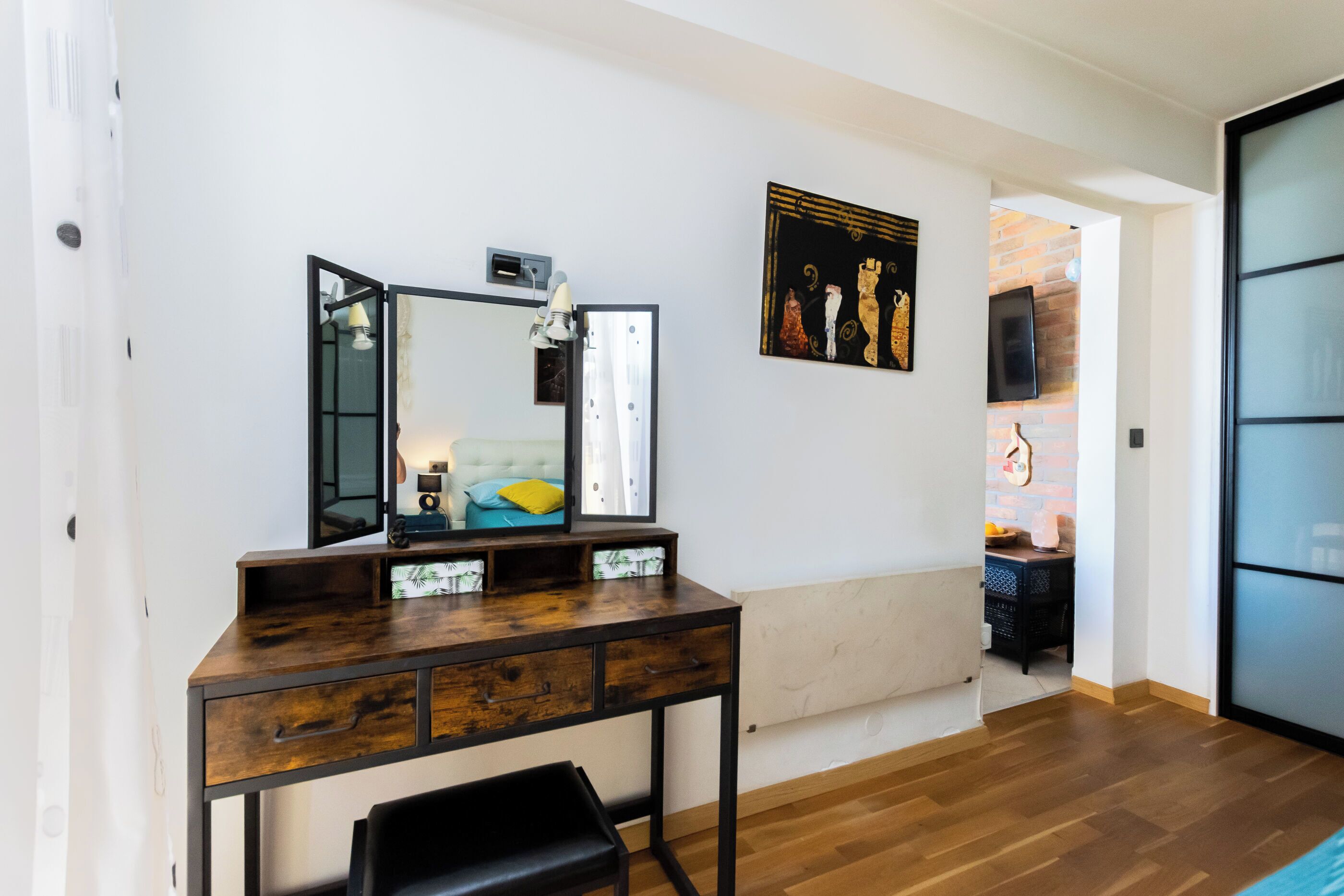 A room with a wooden desk, a chair, a large mirror, and a painting on the wall.