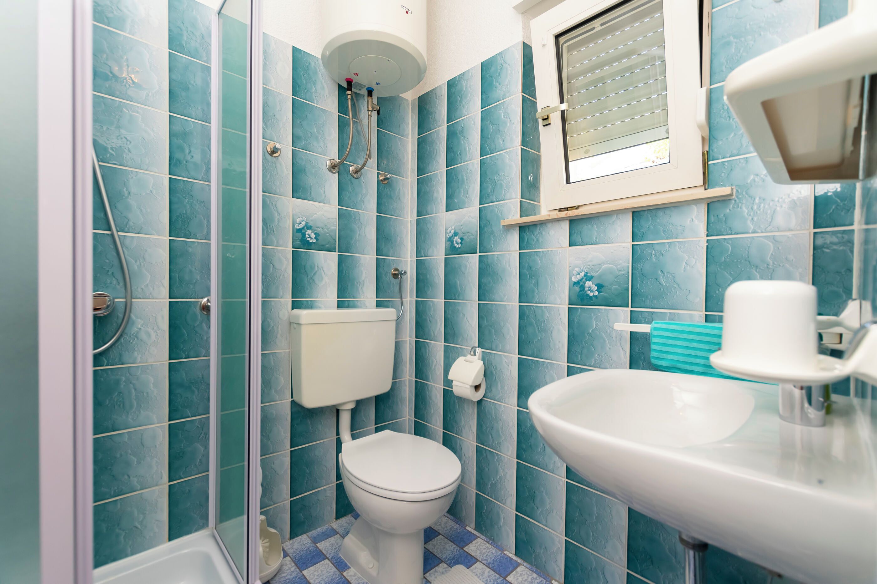 A bathroom with blue tiles, a toilet, a sink, and a shower.