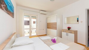 A hotel room with two beds, a wooden headboard, a bedside table with a vase of flowers, a mirror, and a sliding door leading to a balcony. - Apartment Jele (Omis)