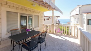 A balcony with a table and chairs, a striped awning, and a view of the sea. - Apartment Jele (Omis)