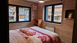 Une chambre à coucher avec un lit, deux fenêtres, une tête de lit en bois et une petite étagère.
