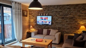 Un salon chaleureux avec un mur en pierre, un téléviseur à écran plat et deux canapés.