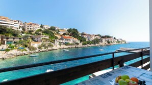 A coastal view with buildings on a hillside, a clear blue sea, and a balcony with fruit. - Apartments First row (Korčula)