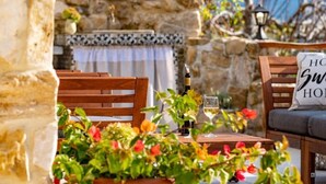 A wooden outdoor seating area with a stone wall backdrop, a bottle of wine, and a glass on the table. - Apartment Filumena (Lopar)