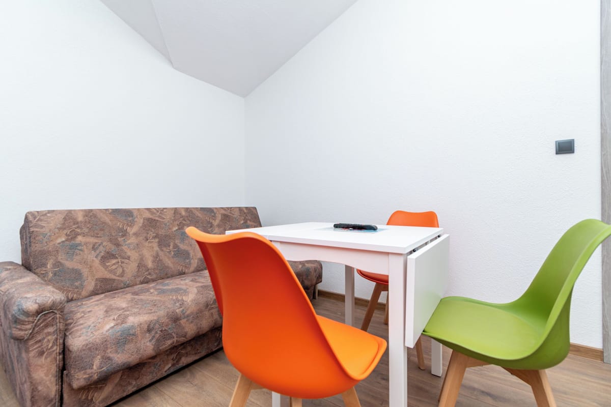 A room with a patterned sofa, a white table, and two chairs, one orange and one green.