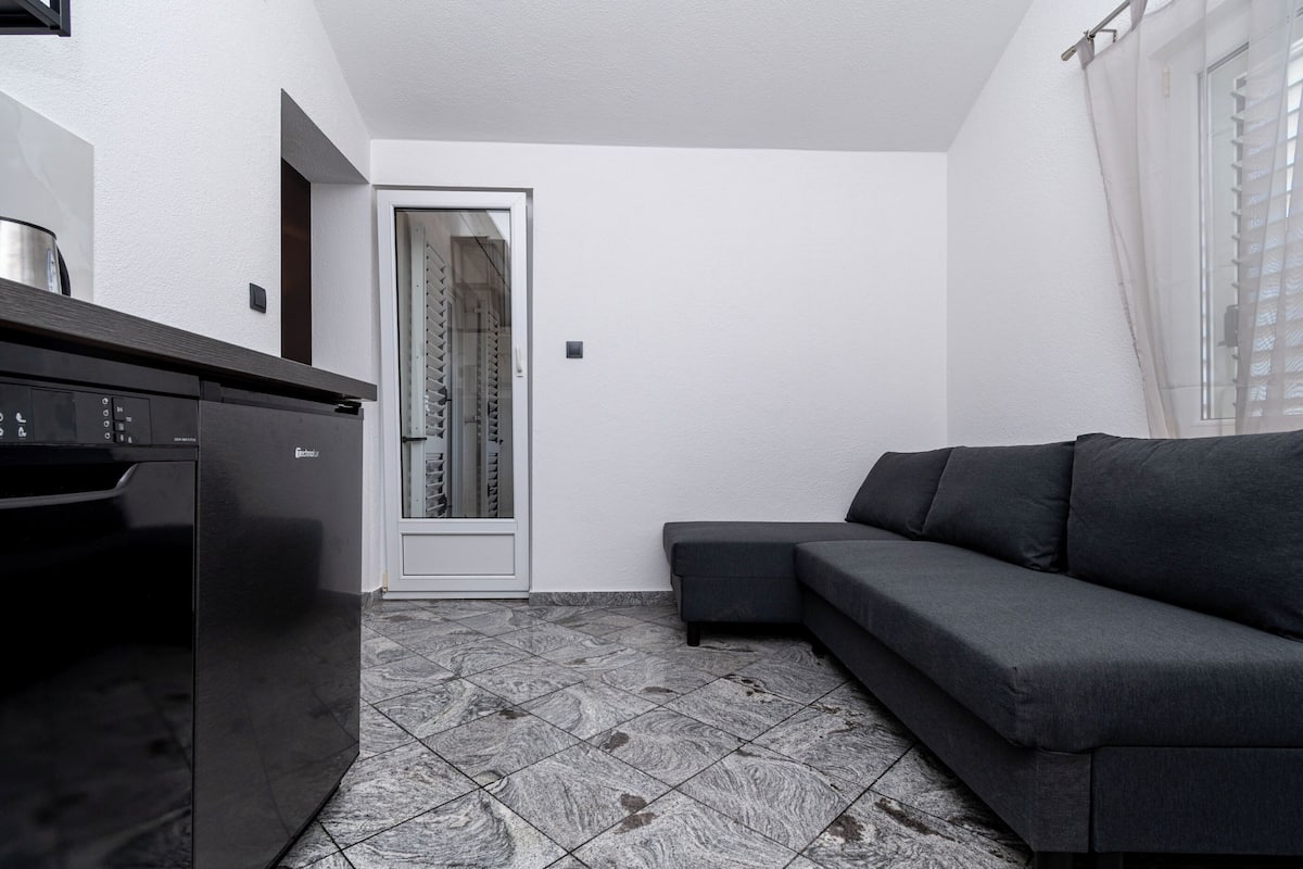 A modern kitchen with a dishwasher, a dark-colored sofa, and a tiled floor.