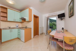 A compact kitchen with teal cabinets, a wooden countertop, and a dining area with a striped tablecloth. - Apartments Villa Vallum (Bol)