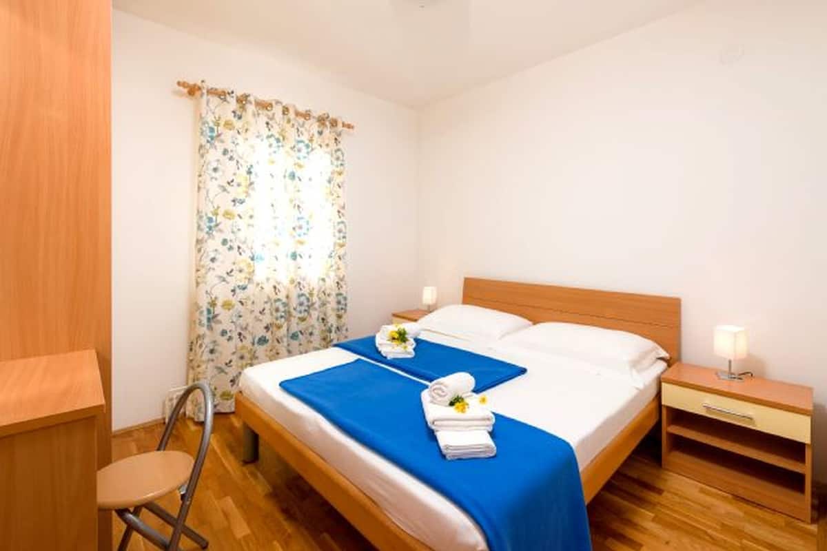 A neatly arranged hotel room with a bed, a chair, a nightstand, and a window with floral curtains.