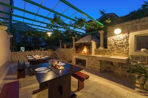 Eine Außenpatio mit Steinmauern, einem Kamin aus Stein und einer Pergola mit hängenden Lichtern.