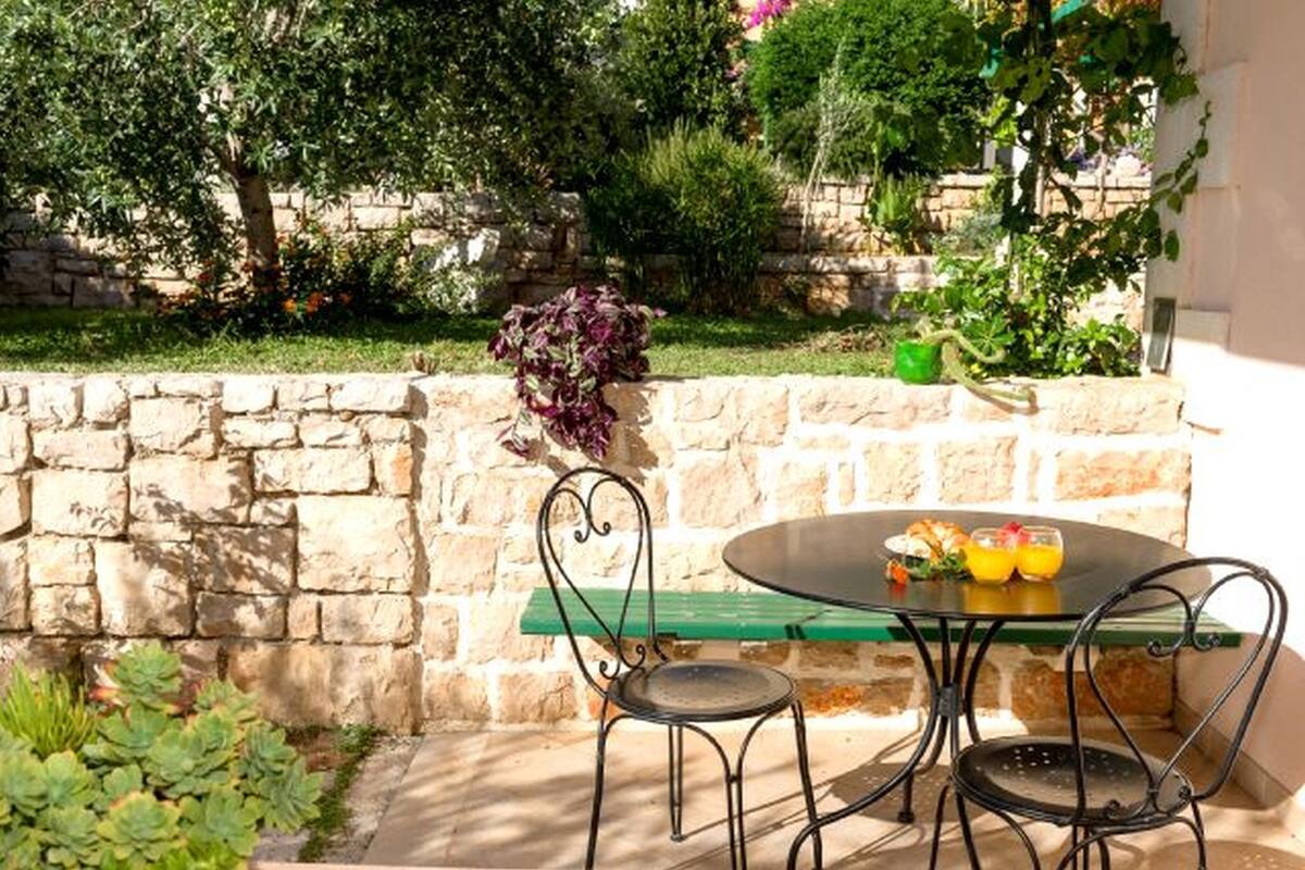 An outdoor patio with a round table and four chairs, surrounded by a stone wall and greenery.