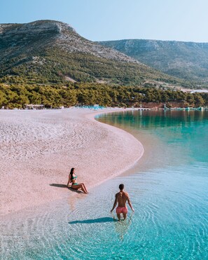 Une plage à l’eau turquoise et limpide, bordée d’un rivage sablonneux, avec une chaîne de montagnes en toile de fond.