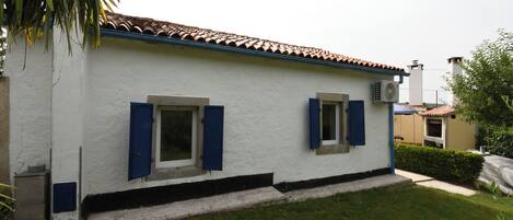 A white building with blue shutters, a tiled roof, and a small front yard.