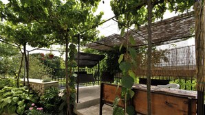 Et udendørs opholdsområde med en træbænk, en stenplanter og et pergola-lignende konstruktion.