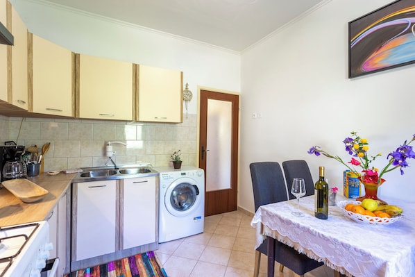 A compact kitchen with a washing machine, a dining area with a table set for two, and a dining chair. - House Gioia Cristina (Labin)