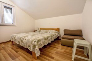 Un dormitorio con cama, mesita de noche, sofá y un taburete blanco pequeño.