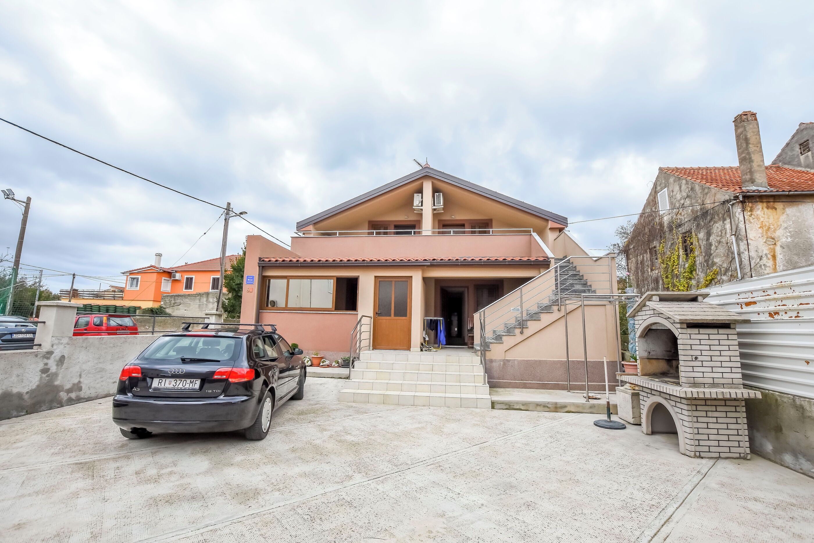Una casa de dos pisos con entrada frontal, una escalera y una estructura de horno de ladrillo.