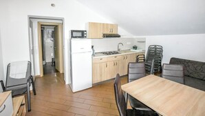 Et kompakt køkken med mikrobølgeovn, komfur og vask, et spiseområde med bord og stole, samt en sofa.