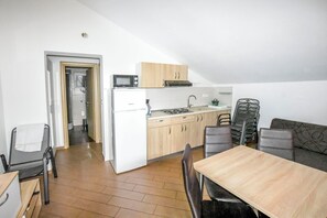 A compact kitchen with a microwave, stove, and sink, a dining area with a table and chairs, and a sofa. - Apartments Ornella (Pasman)