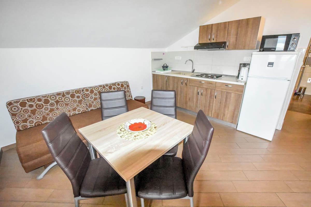 Une cuisine compacte équipée d’un four à micro-ondes, d’une cuisinière et d’un réfrigérateur. On y trouve une table à manger avec quatre chaises et un banc agrémenté d’un coussin à motifs.