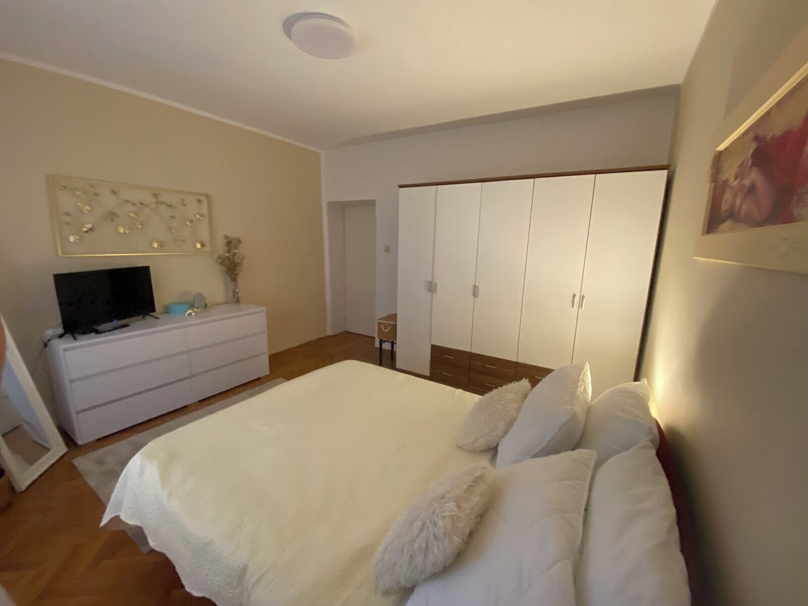 A bedroom with a large bed, a dresser, a television, and a wardrobe.