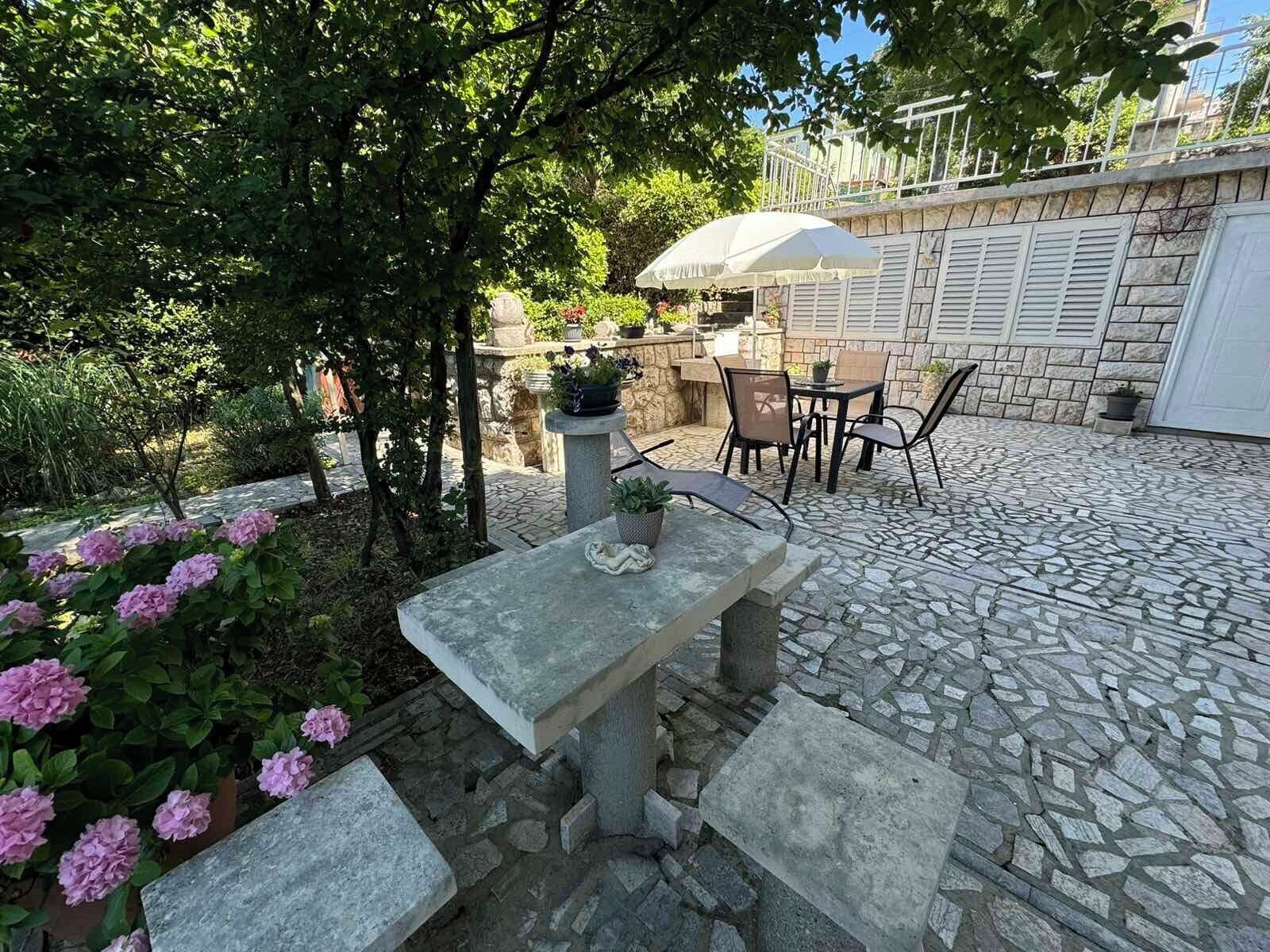 Een terras van stenen met een tafel en stoelen, omringd door bloempotten en bloemen.