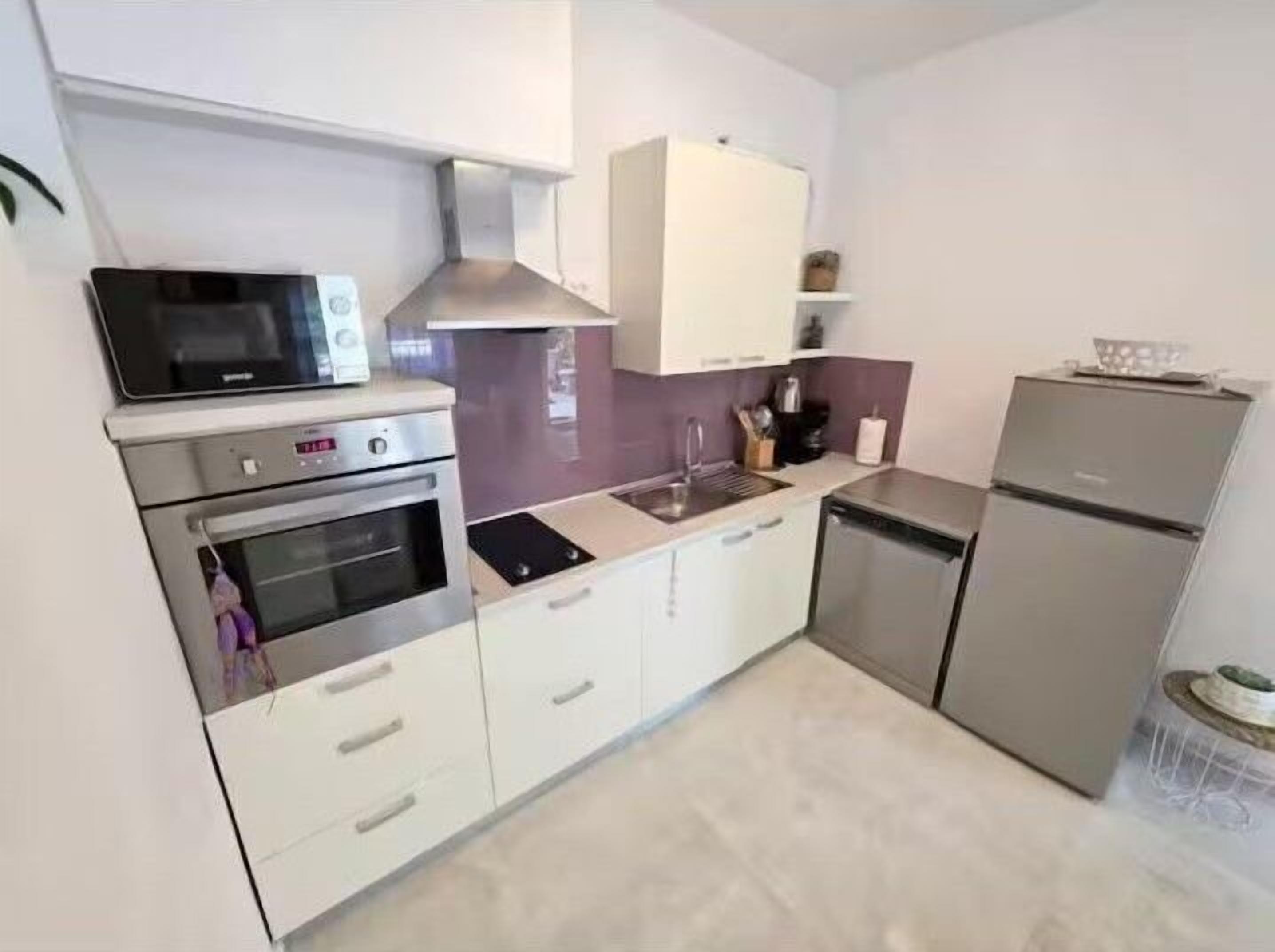 A compact kitchen with white cabinets, a built-in microwave, a stove, a sink, and a refrigerator.